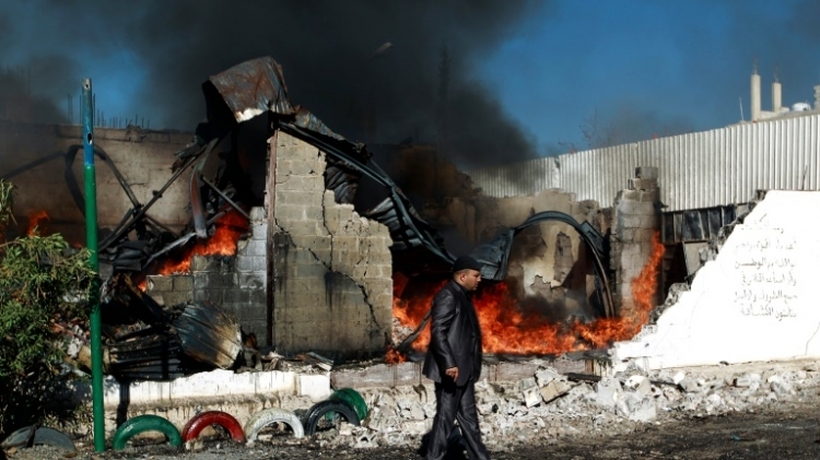 A Yemeni man walks past flames rising from the ruins of buildings destroyed in an air-strike by the Saudi-led coalition in the capital Sanaa, on February 10, 2016